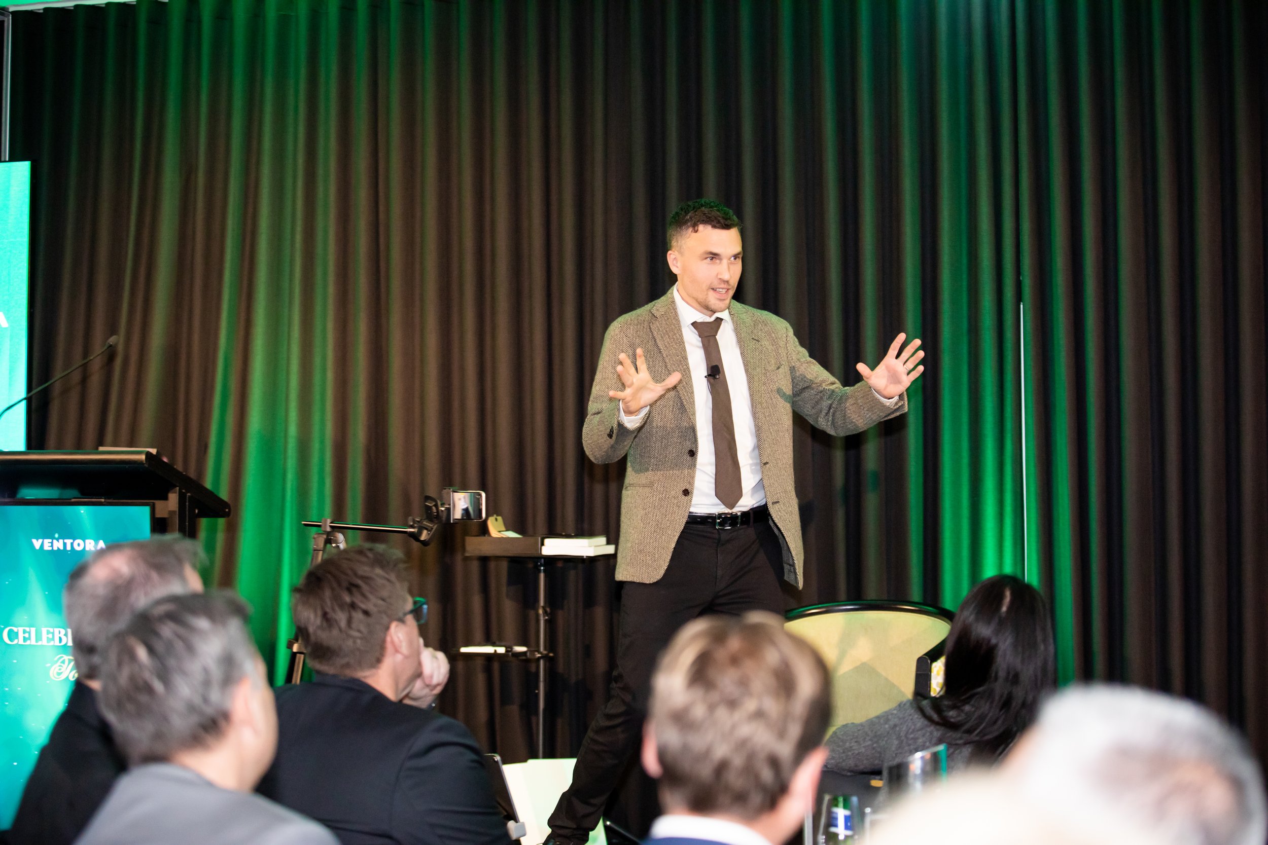 Andy Nunn presenting to a conference audience in a green-lit venue