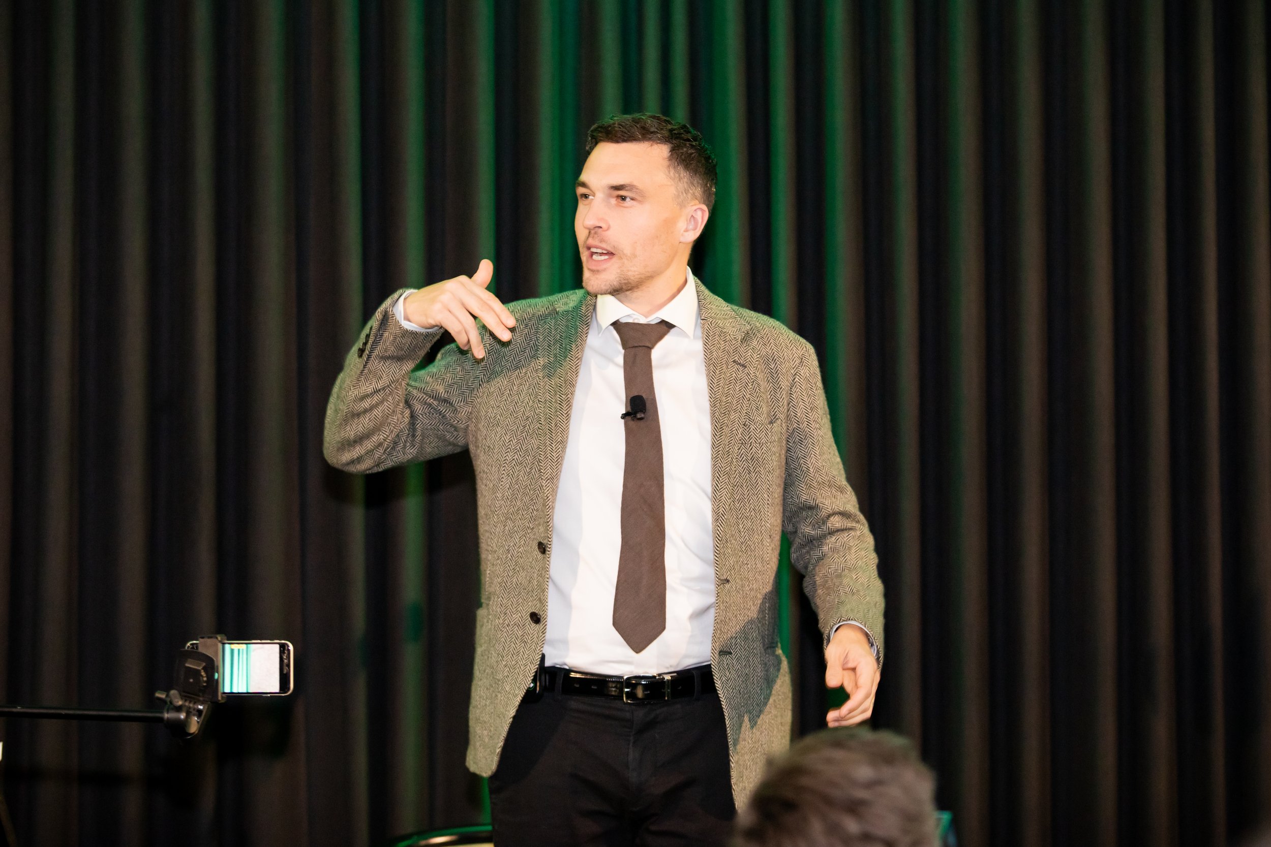 Andy Nunn speaking on stage in front of green curtains